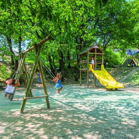 Jeux d'enfants avec toboggan jaune à l'ombre de grands arbres